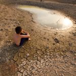Water crisis, Child sit on cracked earth near drying water.
